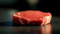 Fresh raw ribeye steak with marbling on wooden surface ready for grilling and cooking in restaurant kitchen or home preparation.