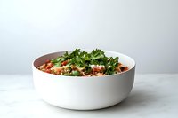 Fresh quinoa bowl garnished with chopped parsley, tomatoes and vegetables served in modern white ceramic bowl on light background.