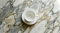 Empty white cup and saucer on marble surface with gold and gray veining, overhead view. Suitable for beverage, café, and lifestyle design projects.