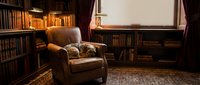 Cozy vintage leather armchair in warm library interior with wooden bookshelves, oriental rug and ambient lighting creating scholarly atmosphere for reading.
