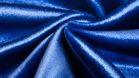 Luxurious royal blue satin fabric with elegant folds and creases creating dramatic light and shadow effects, showcasing smooth textile surface texture and sheen.