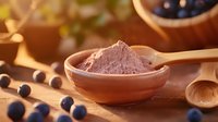 Organic acai berry powder in ceramic bowl with fresh blueberries scattered on wooden surface, warm lighting creates cozy atmosphere for healthy superfood concept.