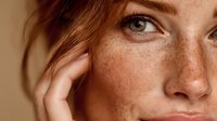 Close-up portrait of young Caucasian woman with natural freckles and auburn hair touching face. Natural beauty skincare concept for cosmetics advertising.