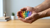 Hands holding colorful paper cutout figures representing diversity, inclusion and community support in workplace or social environment.