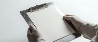 Professional hands in medical gloves holding clipboard with blank paper for healthcare documentation and medical records management.