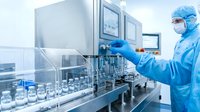 Pharmaceutical technician in protective suit operating sterile filling equipment in modern cleanroom laboratory for drug manufacturing and quality control.