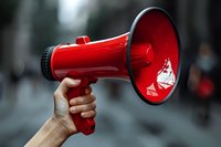 Hand holding bright red megaphone against blurred urban background, powerful communication tool for protests, announcements and public speaking events.
