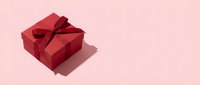 Red gift box with burgundy ribbon on soft pink background for holiday celebrations and special occasions.
