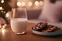 Fresh chocolate chip cookies on gray plate with glass of milk against blurred warm lights background, creating cozy evening atmosphere.
