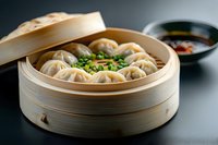 Steamed Asian dumplings with chopped green onions in traditional bamboo steamer basket served with soy dipping sauce on dark background.