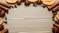 Aromatic winter spices frame wooden background with cinnamon sticks, star anise, cloves and dried orange slices creating festive holiday cooking border.
