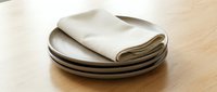 Folded cream linen napkin stacked on ceramic plates against wooden surface, suitable for dining, hospitality, and tableware design projects.