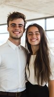 Young diverse couple laughing together in bright office space, wearing white business attire. Natural genuine expressions showcase joy and connection.