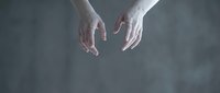 Two open hands reaching downward against soft gray background suggesting help, support, assistance, or offering guidance in minimalist composition.