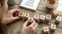 Mental health awareness concept with wooden blocks featuring wellness icons and motivational message on rustic desk with coffee cup.