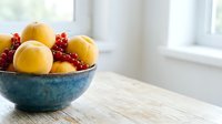 Yellow apples and red currants in a blue ceramic bowl on wooden table near bright window for food styling and kitchen decor.
