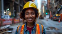 Young African American female construction worker wearing safety helmet and reflective vest smiles confidently at urban worksite during evening hours.