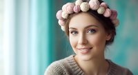 Young Caucasian woman with pink hair rollers in cozy sweater smiling at camera. Beauty routine, hair care and styling preparation concept for salon services.