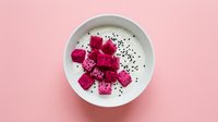 Dragon fruit cubes and edible flowers arranged in white bowl on pink background, overhead view for food styling and culinary design.