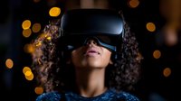 Young woman with curly hair wearing virtual reality headset against dark background with golden bokeh lights, expressing wonder and amazement.