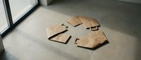 Flat lay of cardboard box pieces and kraft paper packaging materials scattered on concrete floor near window, suitable for shipping, logistics, recycling, and sustainable packaging design projects.