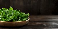 Fresh arugula leaves in wooden bowl on dark rustic background with copy space, healthy green salad ingredient for Mediterranean cuisine.