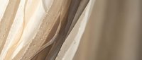 Elegant flowing beige and cream fabric with delicate golden dots creating soft waves and luxurious textile movement for interior design projects.