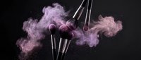 Professional makeup brushes with purple powder explosion on black background for cosmetic advertising and beauty industry marketing campaigns.