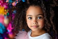 Young African American girl with curly natural hair and bright smile against colorful bokeh background, wearing white. Portrait captures childhood joy and innocence.