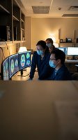 Medical team analyzing brain scans on multiple monitors in modern healthcare facility wearing protective masks during collaborative diagnosis session.