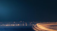 Curved highway light trails at night with glowing orange streaks against dark blue sky, creating dynamic motion effect for transportation and technology concepts.
