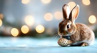 Adorable brown bunny with Easter egg on blue background with golden bokeh lights creating magical holiday atmosphere. Perfect for spring and Easter designs.