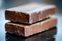 Dark chocolate bars stacked with smooth texture and rich brown color on black surface, macro food photography showing delicate cocoa dusting and layers.