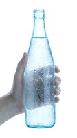 Hand holding chilled glass bottle filled with sparkling water or soda, condensation droplets covering exterior, isolated on white background for beverage advertising.