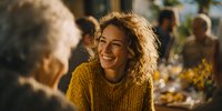 Young woman with curly hair in yellow sweater smiling during family dinner gathering, creating warm atmosphere of connection and joy.