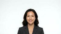 Professional Asian businesswoman in dark suit jacket smiling confidently against white background for corporate headshot and business presentations.