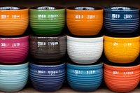 Colorful ceramic bowls with ribbed texture arranged in rows showcase vibrant hues of orange, green, blue, pink, brown, white and yellow. Modern kitchenware display.