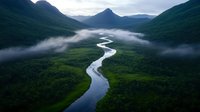 Meandering river flows through misty valley with dramatic mountain peaks and low-lying clouds, aerial view of pristine wilderness landscape in moody atmospheric conditions.