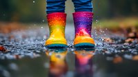 Colorful rainbow rubber boots splashing in puddle with water drops and autumn leaves reflection. Child wearing bright wellington boots on rainy day outdoors.
