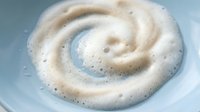 Creamy swirl of foamy milk or cream creating spiral pattern in white bowl, perfect for coffee art, dairy products, and culinary presentations.