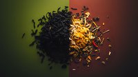 Black and golden tea leaves scattered on dark background with dramatic lighting and color gradient, creating artistic food composition for beverage advertising.