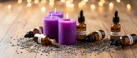 Purple candles with essential oil bottles and lavender seeds on wooden surface with warm bokeh lights for aromatherapy spa relaxation wellness treatment.
