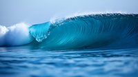 Powerful turquoise ocean wave breaking with white spray against blue sky. Dynamic water movement captures raw force of nature in tropical seascape.