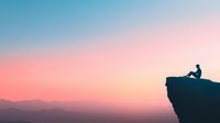 Silhouette of person sitting on cliff edge against colorful sunset sky and mountain landscape, peaceful solitary moment capturing freedom and achievement.