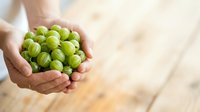 Hands holding fresh green gooseberries on wooden surface, ideal for food, agriculture, and healthy eating content.