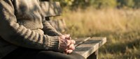 Senior man in warm sweater sitting peacefully on wooden bench outdoors during golden hour autumn day reflecting in nature park setting.