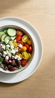 Fresh Greek salad bowl with cherry tomatoes, cucumber, olives, feta cheese, and red onion on a wooden table, top view.