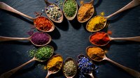 Colorful spices and herbs arranged in wooden spoons on dark slate background. Cooking ingredients for seasoning and flavoring dishes in kitchen.