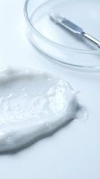 Cosmetic cream sample with glass petri dish and metal spatula on white background, suitable for skincare product marketing and beauty packaging design.