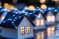 Miniature house models with glowing windows connected by blue light network lines against blurred bokeh background illustrating smart home technology concept.